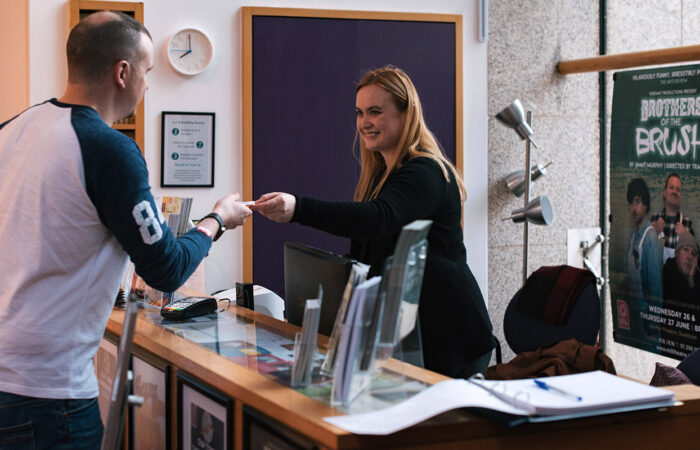 A staff member at the box office handing out tickets performance at dlr Mill Theatre