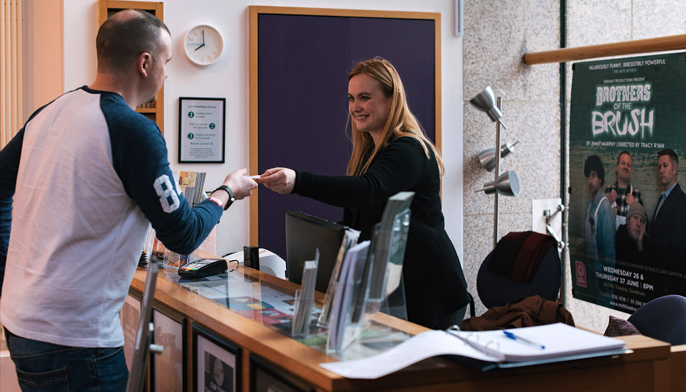 A staff member at the box office handing out tickets performance at dlr Mill Theatre